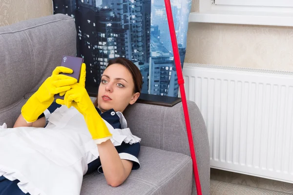 Lazy young housekeeper or maid relaxing on a sofa — Stock Photo, Image