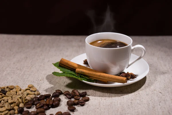 Hot coffee in cup with cinnamon sticks and beans — Stock Fotó