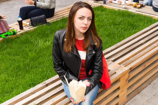 Jovem mulher no banco com take out recipiente de comida — Fotografia de Stock