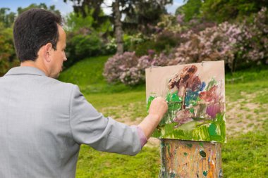Bir erkek sanatçı resim son rötuşları bir parkta yan görünüm