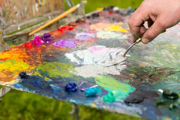 Hand of a male artist mixing white paint on an old palette outdo