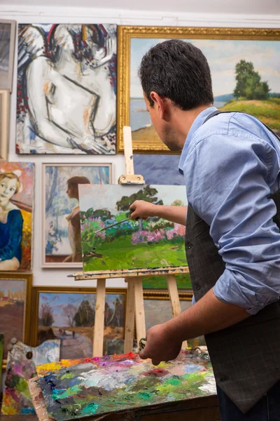 Pintor guapo trabajando en un caballete en un estudio — Foto de Stock