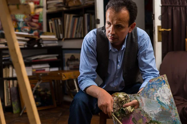 Artist sitting looking at his canvas in a studio — Stock Photo, Image