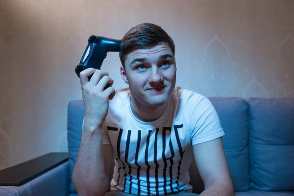 Pensive male gamer scratch his head by console — Stock Photo, Image