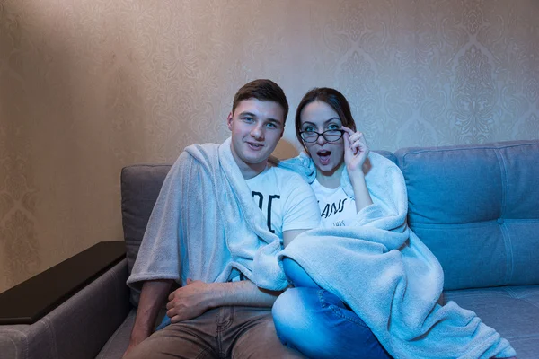 Surprised young boy and girl in glasses snuggling up watching te — Stock Photo, Image