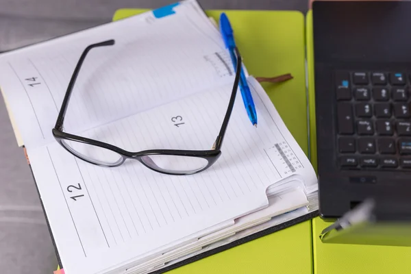 Ζευγάρι γυαλιά και ένα στυλό πάνω σε ένα περιοδικό που βρίσκεται στο τραπέζι laptop — Φωτογραφία Αρχείου