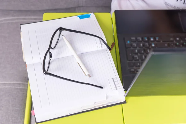 Glasses and a pen on a journal lying on the laptop table — Stock Photo, Image