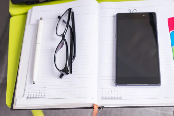 Óculos elegantes que jazem perto do telefone celular na mesa do laptop — Fotografia de Stock