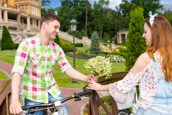 Joven hombre da a una chica flores mientras están montando en bicicletas en — Foto de Stock