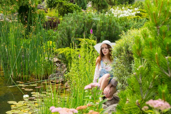 Vrouw in witte hoed zittend op een rots in de buurt van het meer — Stockfoto