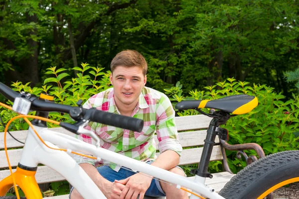 Jongeman zit op een bankje in de buurt van fiets — Stockfoto