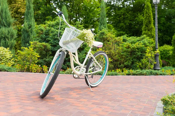 Женский белый велосипед на тропинке с букетом в корзине — стоковое фото