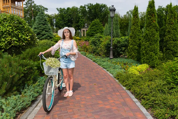 Mulher atraente usando um chapéu branco em pé perto de sua bicicleta — Fotografia de Stock