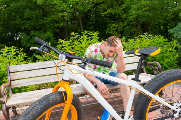 Young man with sad expression sitting on bench near bike — Stock Photo, Image