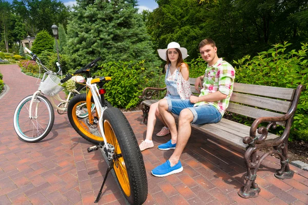 Pár ül a padon, közel a gyönyörű zöld parkban kerékpárok — Stock Fotó