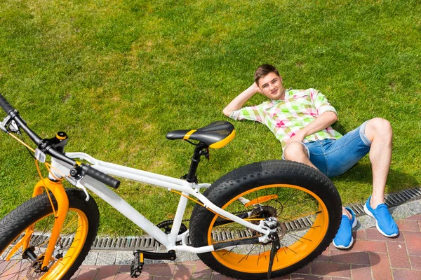Jonge man vaststelling van op gras naast de fiets — Stockfoto