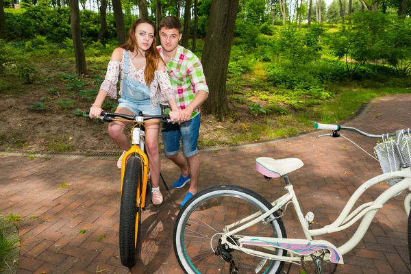 Handsome male teaches his girlfriend riding a bicycle in a park — Stock Photo, Image