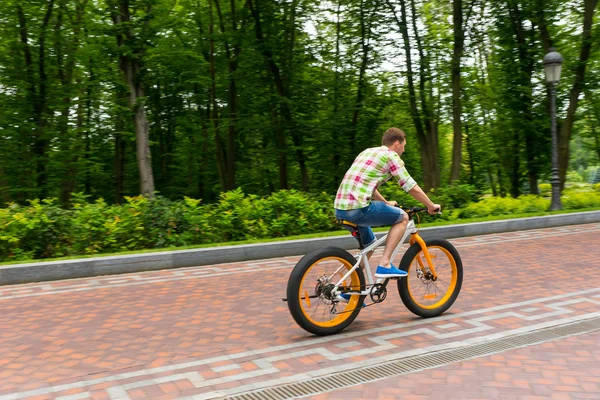 Jovem montando uma bicicleta em um caminho no parque — Fotografia de Stock