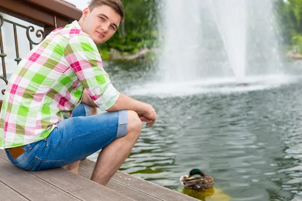 Młody człowiek, karmienie kaczek w stawie — Zdjęcie stockowe