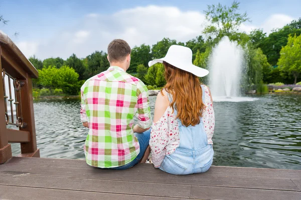 Young couple sitting on the wooden deck and feeding ducks in a p — Stock Photo, Image