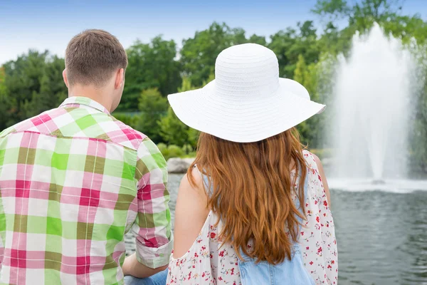 Joven hombre y mujer sentado frente al lago artificial en un pa —  Fotos de Stock