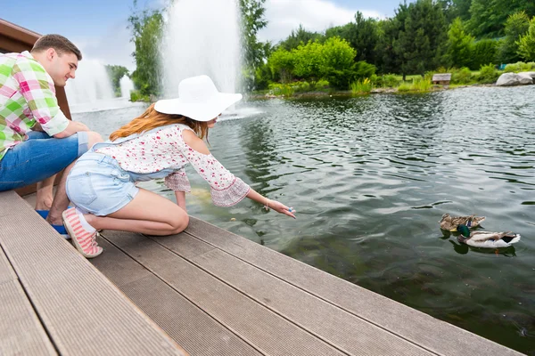 Jovem mulher alimentando patos em uma lagoa — Fotografia de Stock