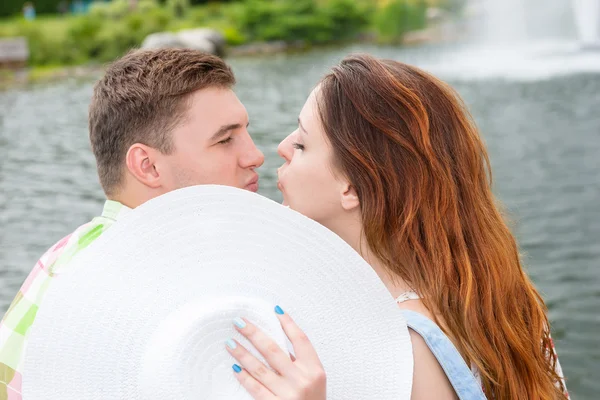 Ung man och kvinna kysser gömma sig bakom hatten — Stockfoto