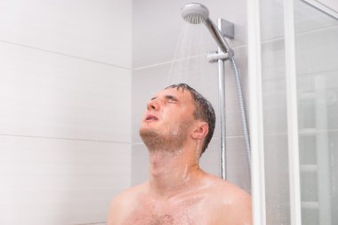Young man with closed eyes taking a shower in the bathroom