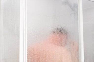 Young man taking a shower standing behind transparent misted gla clipart