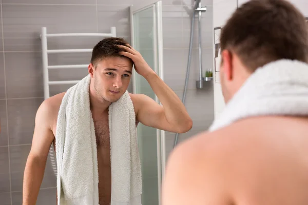 Young man holding towel on his shoulders while looking in the mi — Stock Photo, Image