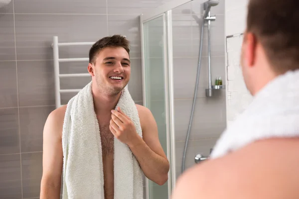 Feliz hombre sonriendo, sosteniendo la toalla en sus hombros después de lavarse — Foto de Stock