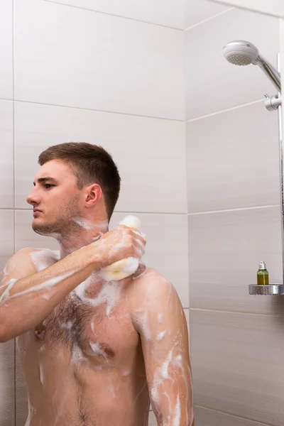 Nu jovem masculino esfregando-se um espuma esponja banheira no chuveiro cabine — Fotografia de Stock