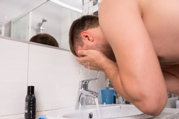 Adam banyoda yüzüne su püskürtme — Stok fotoğraf