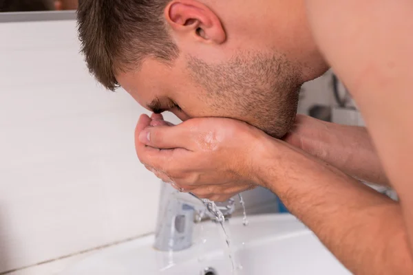 Cerca de hombre joven lavando la cara en el baño — Foto de Stock