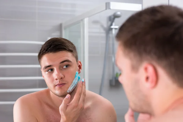 Bonito jovem esfregando gel de barbear em seu rosto — Fotografia de Stock