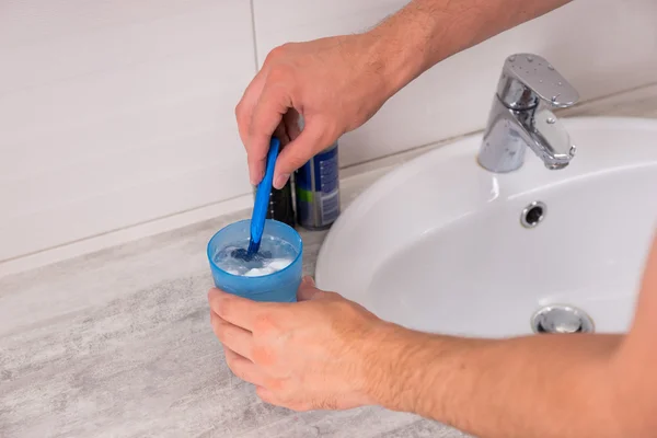 Мужские руки, моющие бритву в чашке с водой — стоковое фото
