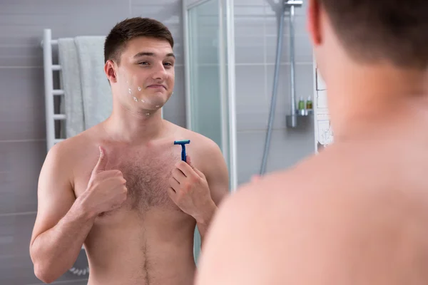 Happy young man with cuts on his face holding a razor — Stock Photo, Image