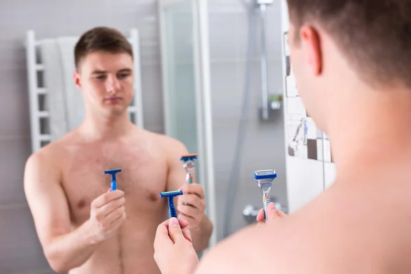 Macho sosteniendo máquinas de afeitar y elige el mejor mientras está de pie en el — Foto de Stock