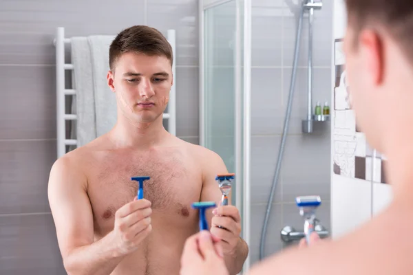 Handsome young male holding razors and chooses the best while st — Stock Photo, Image