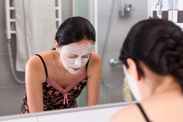 Mujer joven con máscara cosmética lavando la cara de pie delante de —  Fotos de Stock