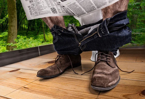 Adult male reading newspaper while sitting on the toilet seat — Stock Photo, Image