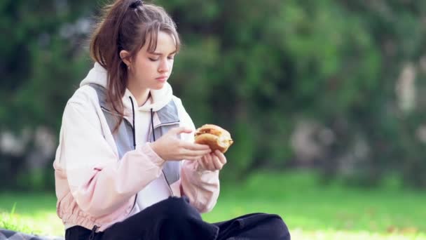 Νεαρή γυναίκα να χαλαρώνει σε ένα χαλί σε ένα πάρκο τρώγοντας — Αρχείο Βίντεο