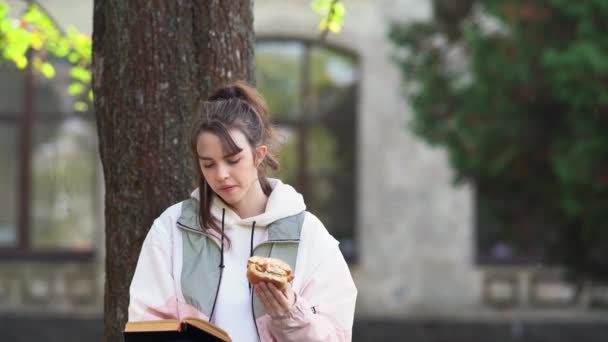 Genç kız oturup okuyor ve yiyor. — Stok video