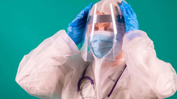 The doctor puts on a face shield wearing a PPE suit uniform with stethoscope on the shoulder and medical protective Mask