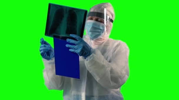 Доктор у костюмі PPE, щит особи і маска перевіряє пацієнта на рентгенівському знімку як тест на Ковді і робить нотатки на зеленому фоні. — стокове відео