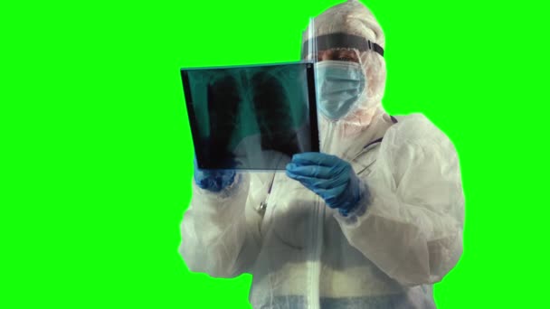 El médico que usa un traje de PPE, un protector facial y una máscara está inspeccionando una radiografía de los pulmones de los pacientes con una cacerola como prueba en Covid, sobre fondo verde. — Vídeos de Stock