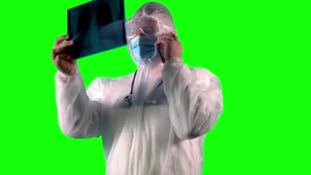 Γιατρός φορώντας ένα κοστούμι PPE, ασπίδα προσώπου και μάσκα είναι επιθεώρηση των ασθενών X-ray των πνευμόνων ως δοκιμή σε Covid, ενώ μιλάμε σε ένα τηλέφωνο, σε πράσινο φόντο — Αρχείο Βίντεο