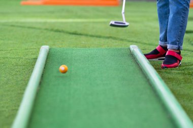 Dışarıdaki sahada minyatür golf oynarken topu sopayla oynayan kişi, sahte uzayın düşük açılı anonim görüntüsüyle yapay yeşil çim kullanıyor.