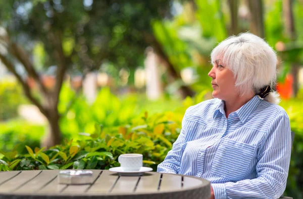 緑豊かな植物に囲まれた屋外のパティオでリラックスした魅力的な中年の女性は コーヒーやお茶のカップを楽しんでいます — ストック写真