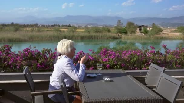 Orta yaşlı bir kadın balkonda şarap ve kahveyle eğleniyor. — Stok video